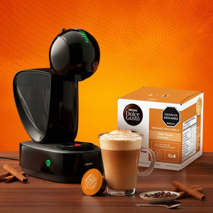 maquina nescáfe dolce gusto con mochaccino canela en taza y caja de cápsulas sobre fondo naranja